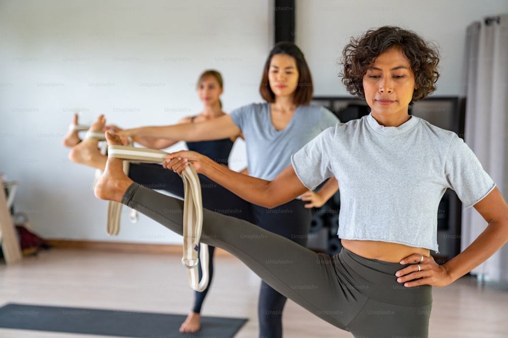 Group of Healthy Asian woman in practicing yoga workout training with using yoga equipment for body stretching fitness exercise together in yoga gym studio. Attractive female friends enjoy indoor activity sport lifestyle.
