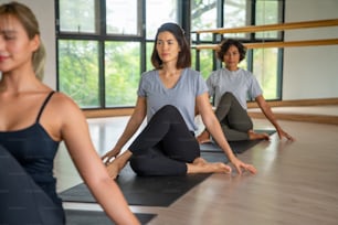 Group of Healthy Asian woman in yoga clothes practicing yoga workout and body stretching fitness exercise together in yoga gym studio. Attractive female friends enjoy indoor activity sport lifestyle