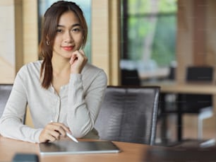 Retrato de mujer de negocios sonriendo en el espacio de trabajo con tableta, lápiz óptico y fondo de oficina
