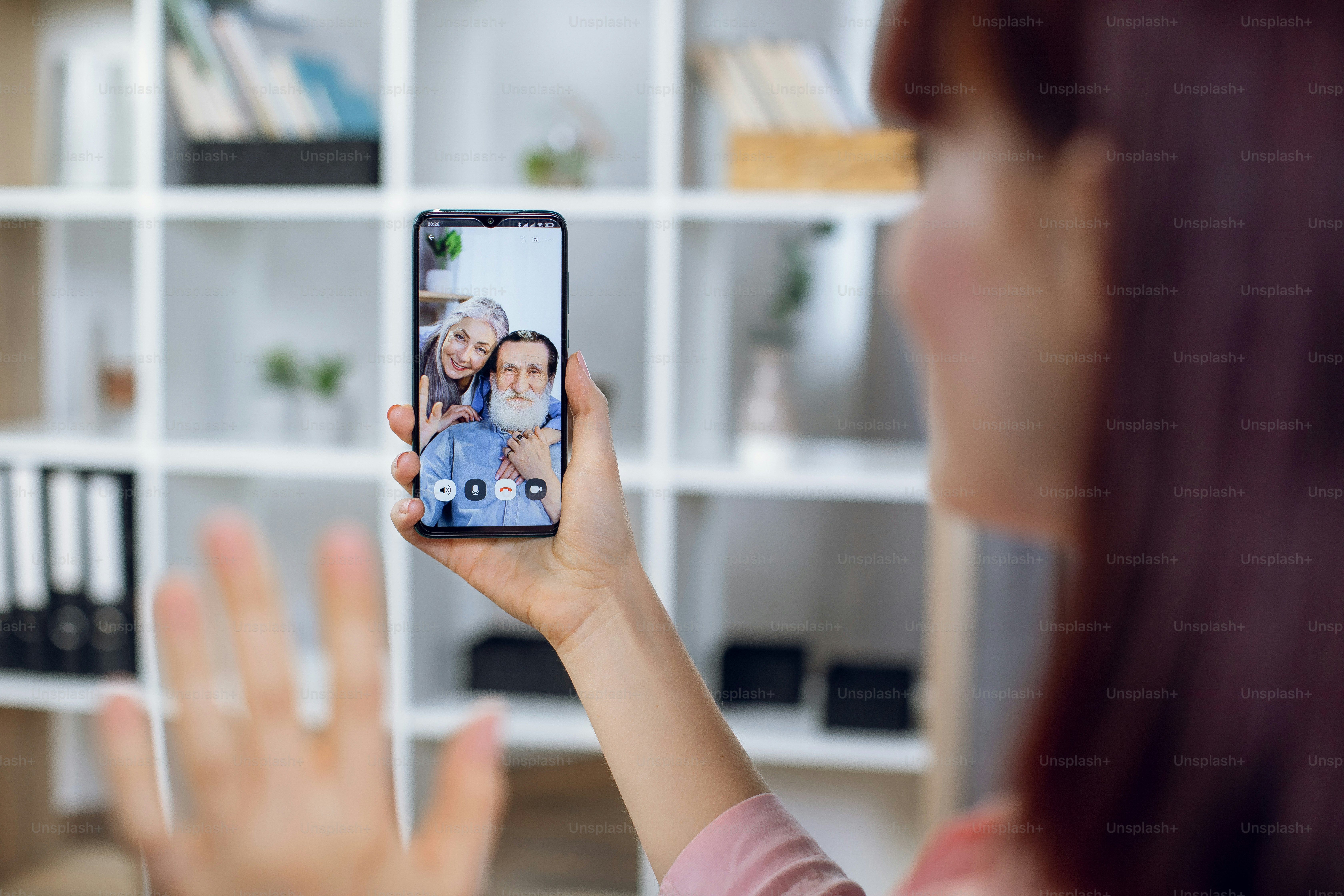 Eine Person, die auf einen Smartphone-Bildschirm winkt, der einen Videoanruf mit zwei Erwachsenen zeigt