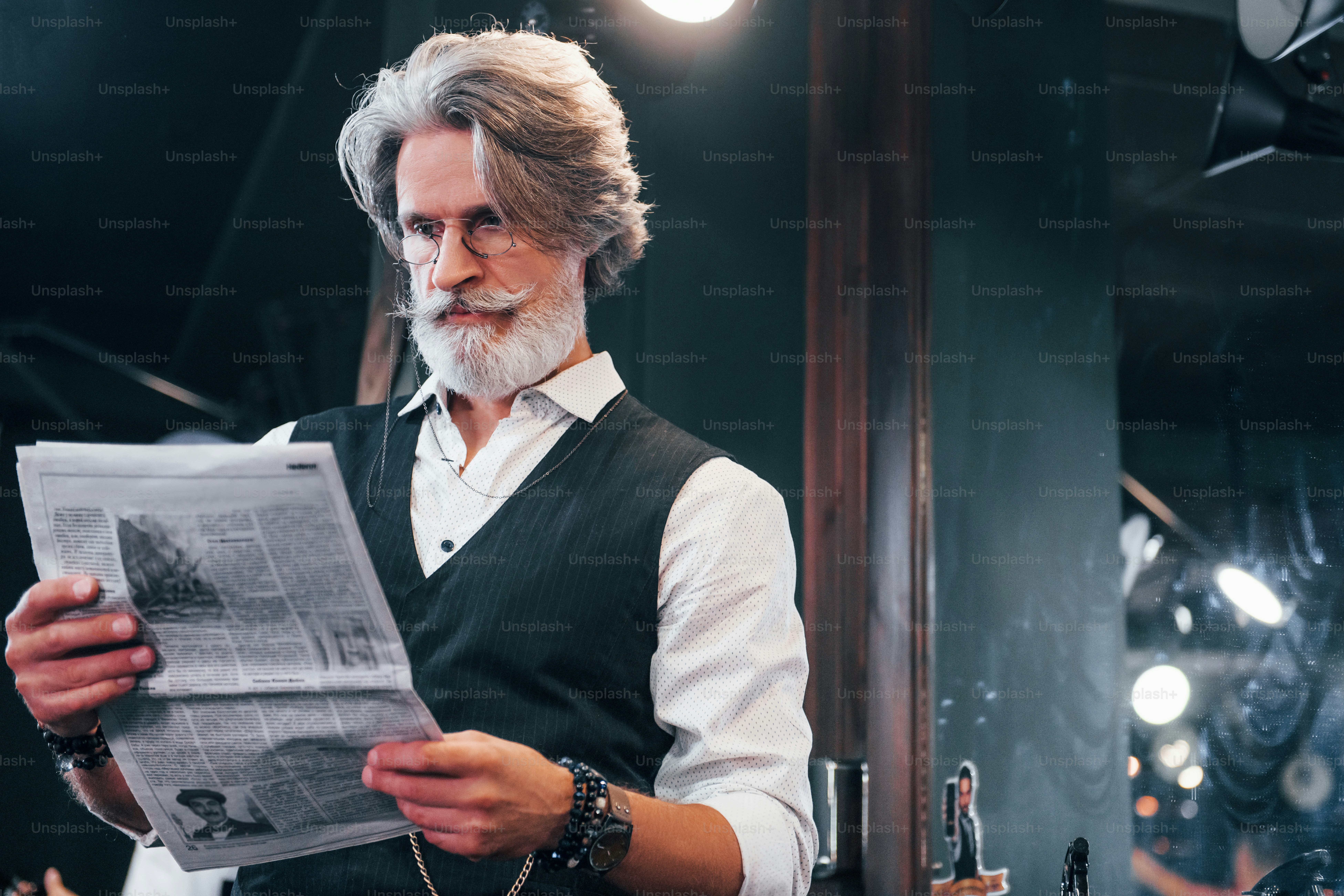 Lectura de periódicos. Elegante hombre mayor moderno con cabello gris y barba está en el interior