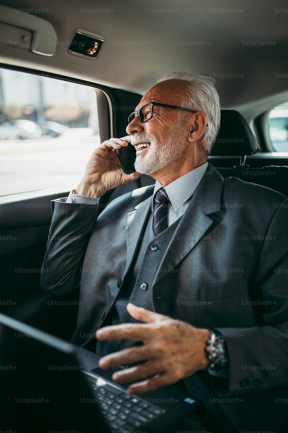 Gut aussehender älterer Geschäftsmann sitzt auf dem Rücksitz in einem Luxusauto. Er benutzt seinen Laptop und reagiert emotional. Transport im Unternehmenskonzept.