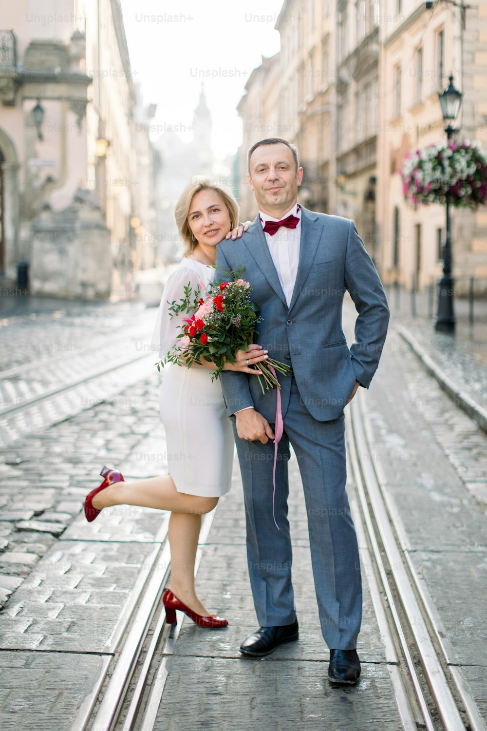 Wedding anniversary 25th celebration. Outdoor portrait of charming mature couple man and woman in elegant luxury clothes, posing together on tram railroad in ancient old city center