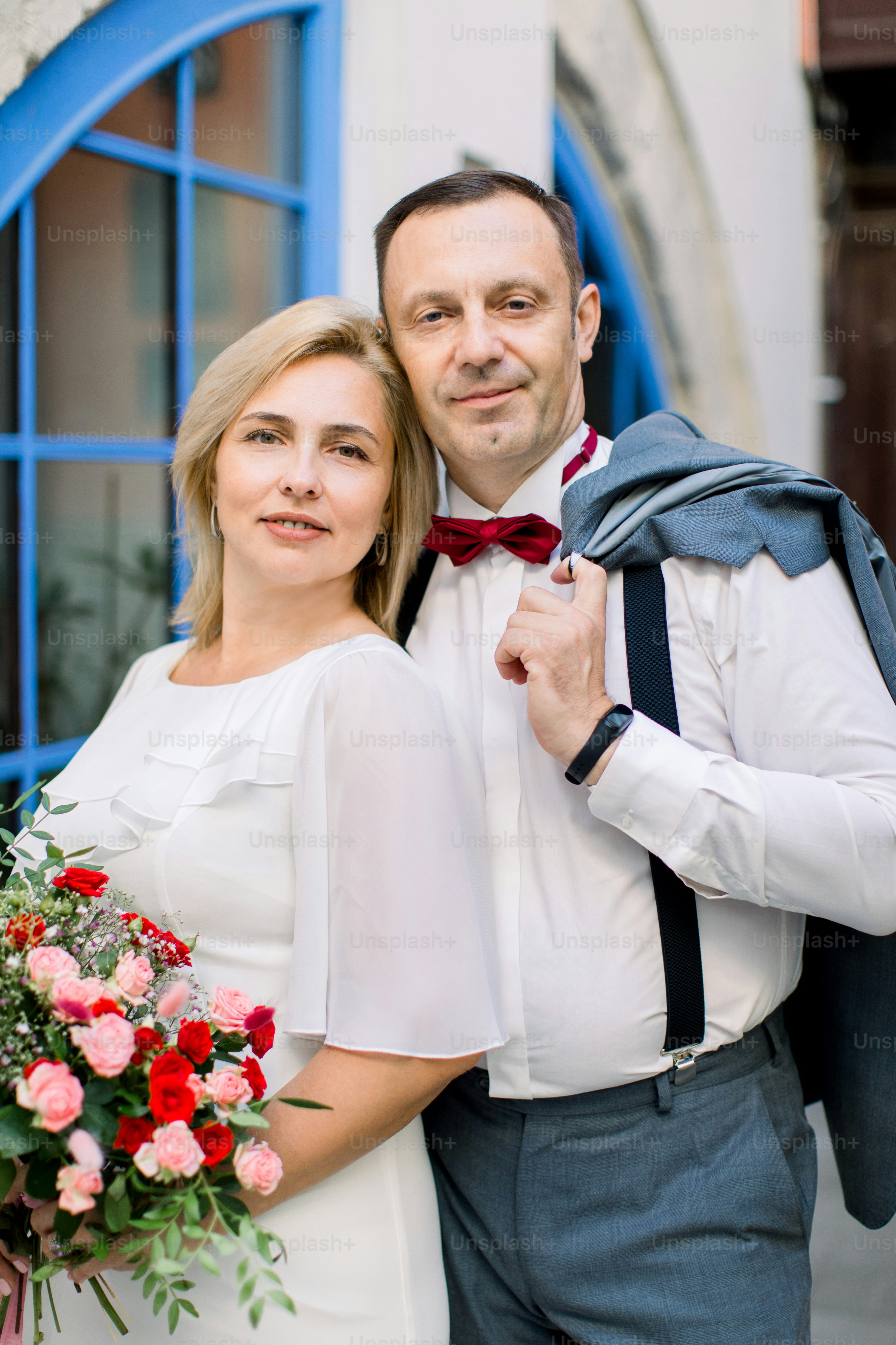 Beau rendez-vous dans la rue. Couple mûr heureux, bel homme avec sa jolie dame en robe blanche, étreignant à l’extérieur dans la ville, posant près de belles fenêtres bleues vintage