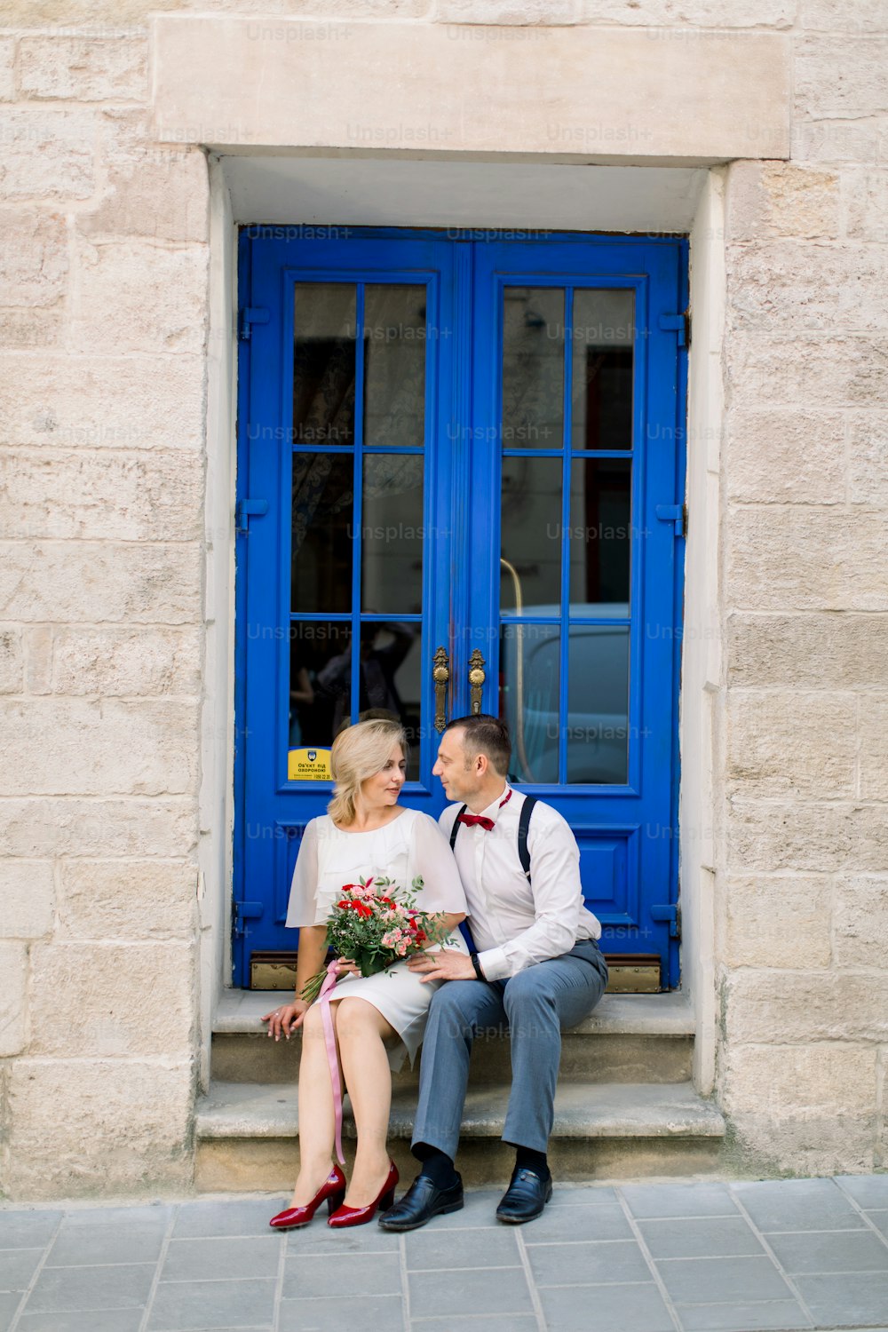 Lovely date on the street. Happy mature loving couple, handsome man with his charming wife in white dress, hugging outdoors in the city, sitting near beautiful vintage blue door