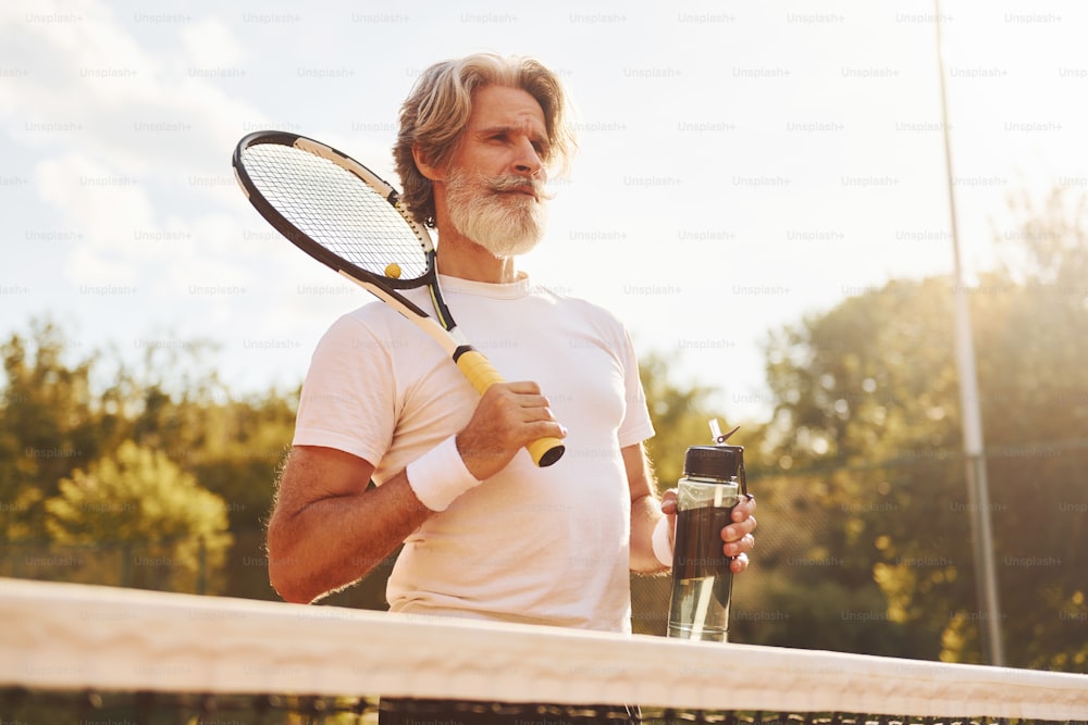Raquete de contenção. Homem elegante moderno sênior com raquete ao ar livre na quadra de tênis durante o dia.