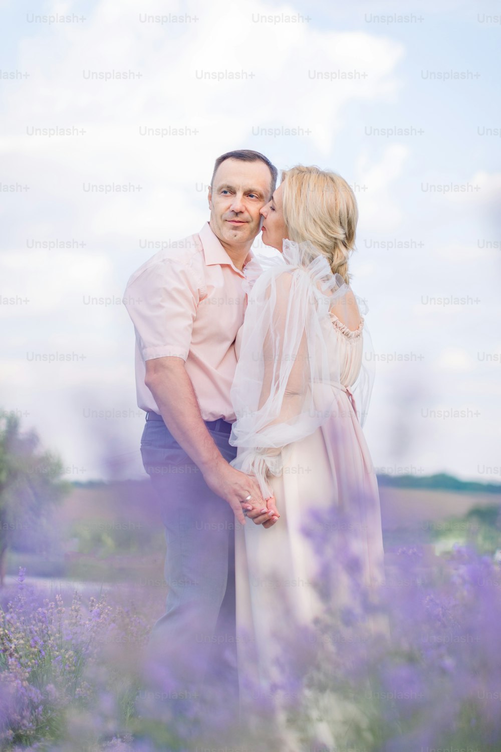 Blick durch die Lavendelblüten. Glückliches Paar mittleren Alters, Mann und Frau in eleganten Outfits, umarmen und genießen romantische Momente zusammen im Lavendelfeld