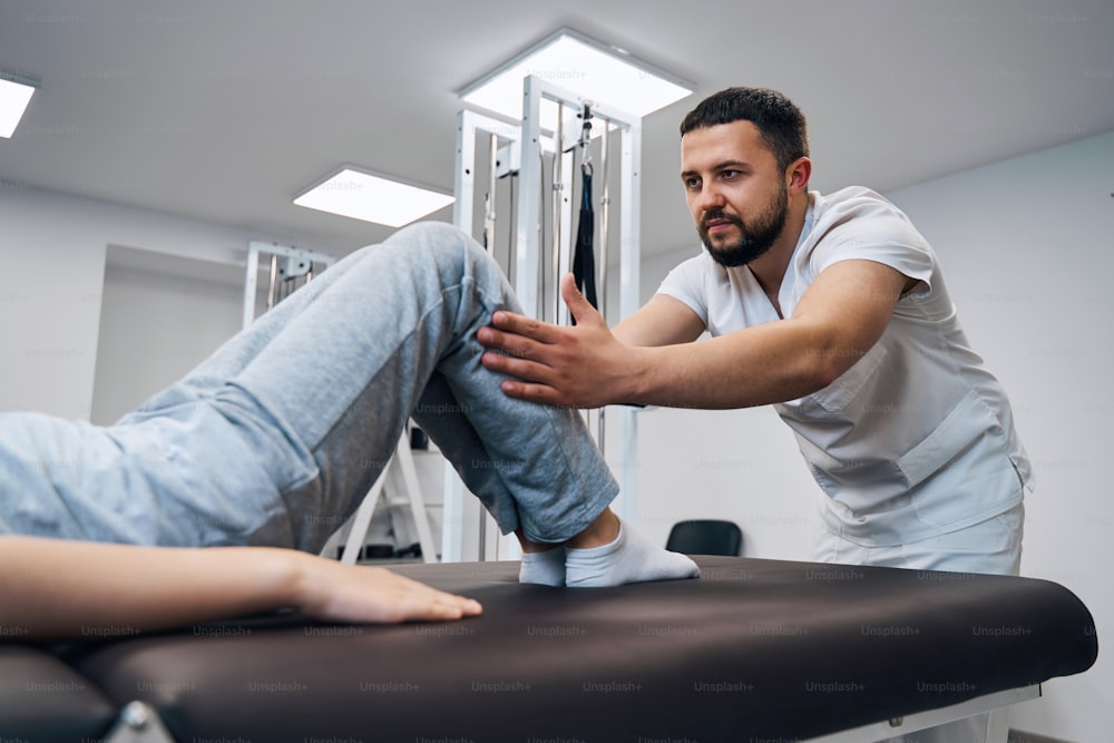 Specialist physiotherapist treats kids knee on massage bed. Physical therapy and health care of sport injury. Chiropractor checks patients feet. Manual therapist works in rehabilitation center