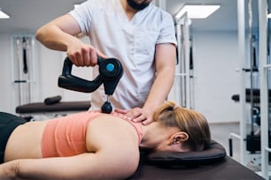 Physiotherapist treats woman spine and back with massaging percussion device. Physio therapy after spinal trauma or sport injury. Scoliosis problem chiropractic treatment. Healthcare and recovery