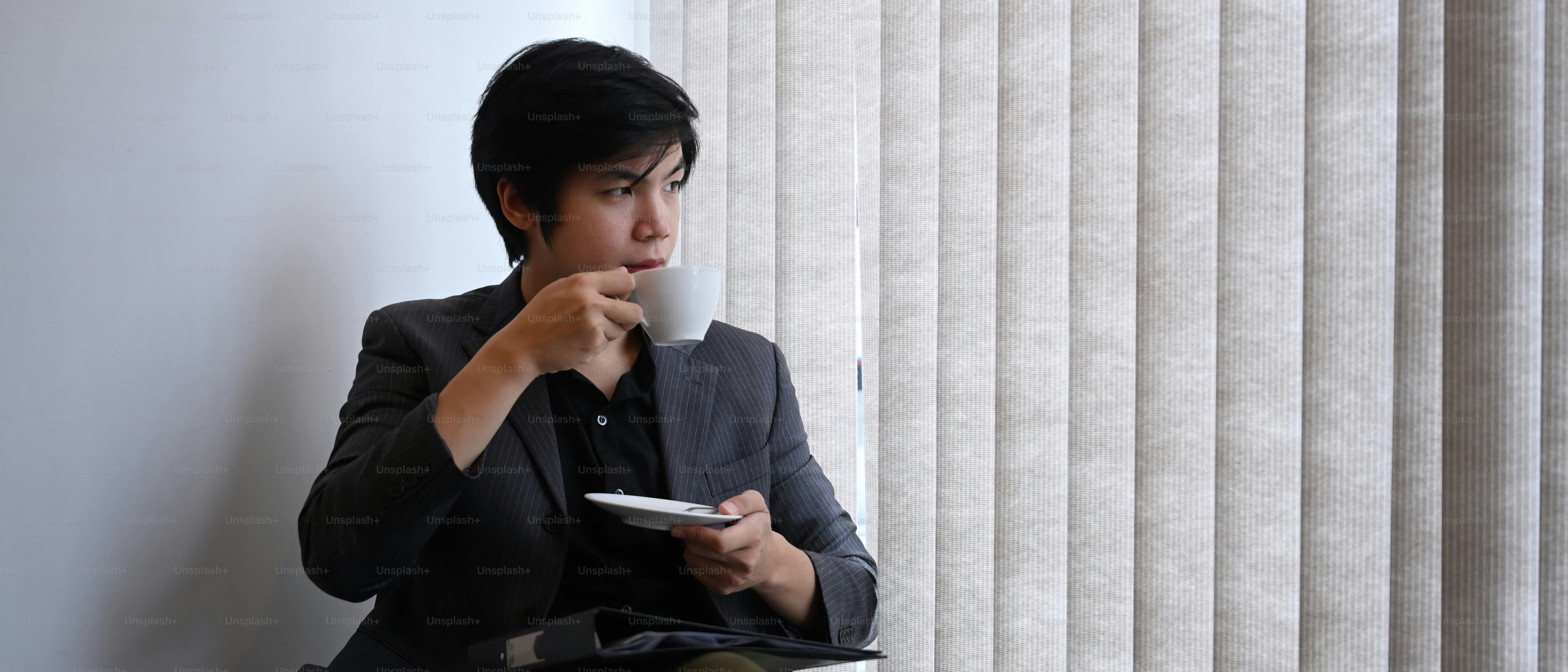 Hombre de negocios reflexivo bebiendo café y mirando a través de la ventana de la oficina.