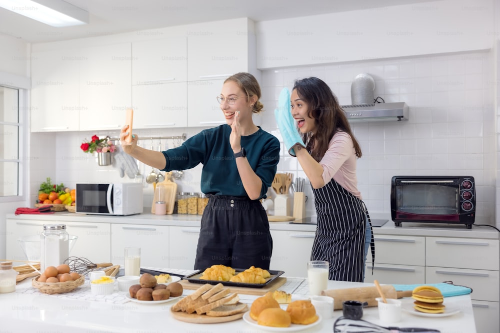 Two female pals are having fun while taking a selfie breakfast in the kitchen.