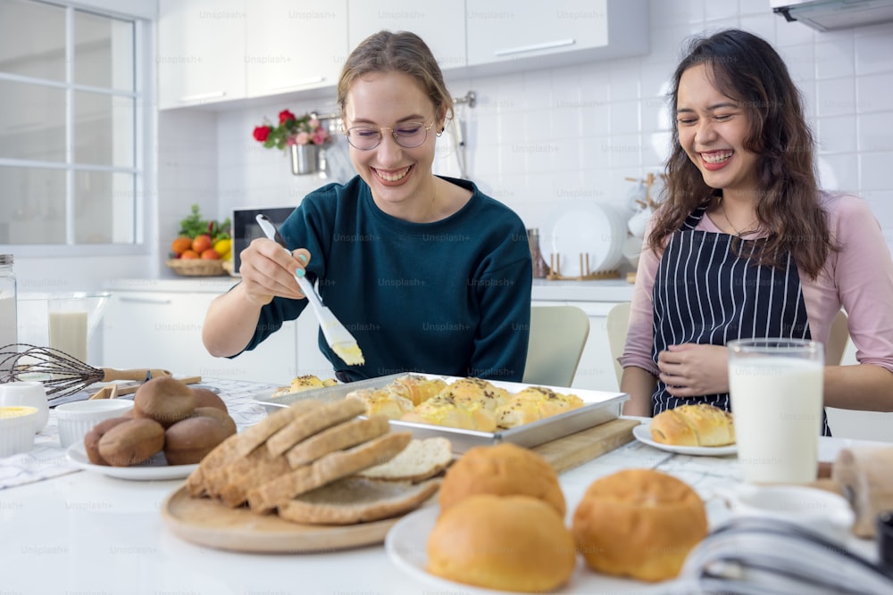 Lindas dos felices, hermosas panaderas horneando dulces Las mujeres se divirtieron en una lección de elaboración de pan y usan sus manos para golpear la masa en la cocina para hacer pasteles juntas.