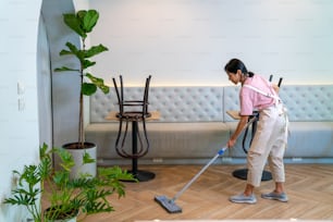 Young Asian woman coffee shop barista cleaning cafe before opening. Female waitress preparing bistro restaurant for service to customers. Small business owner and part time job working employee concept