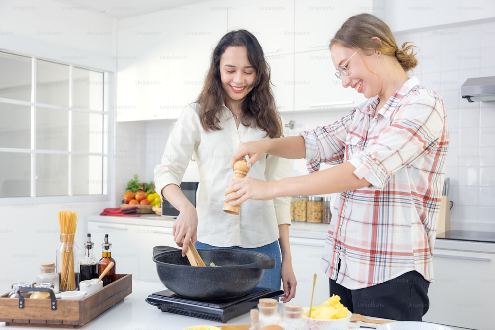 In the kitchen, two happy young twin sisters are preparing spaghetti for lunch.