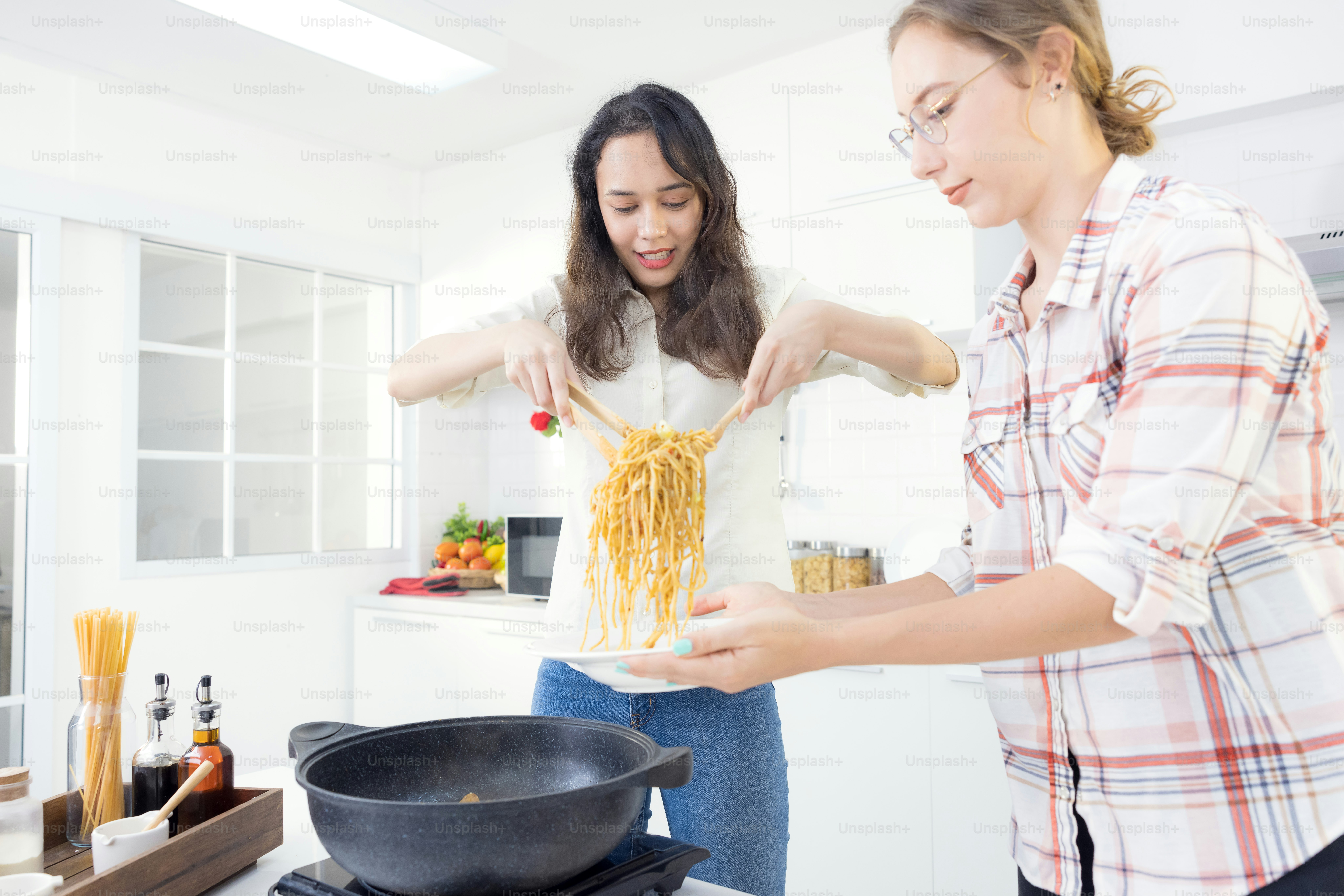 In the kitchen, two happy young twin sisters are preparing spaghetti for lunch.