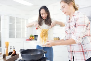 In the kitchen, two happy young twin sisters are preparing spaghetti for lunch.