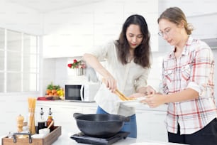 En la cocina, dos felices hermanas gemelas preparan espaguetis para el almuerzo.