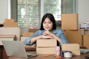 Young happy asian business woman owner of business online using laptop receive order from customer with parcel box packaging at her startup home office, online business seller and delivery