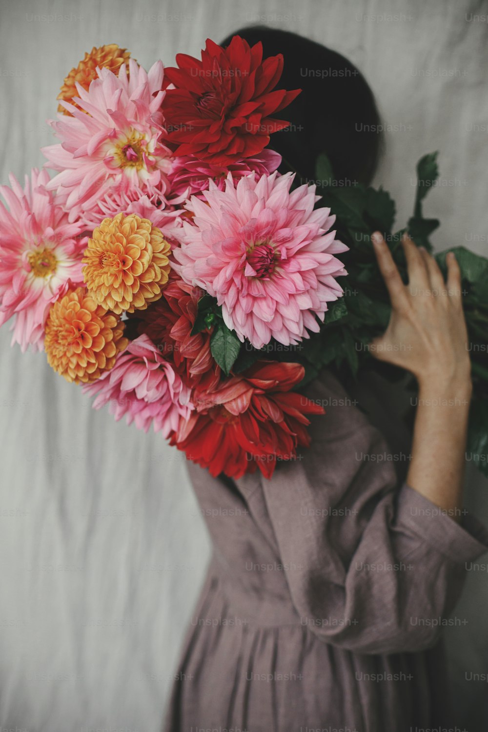 Bella donna che tiene il mazzo di fiori autunnali in una stanza rustica. Immagine estetica atmosferica. Fioraio in abito di lino che si nasconde dietro bellissime dalie colorate. Stagione autunnale in campagna