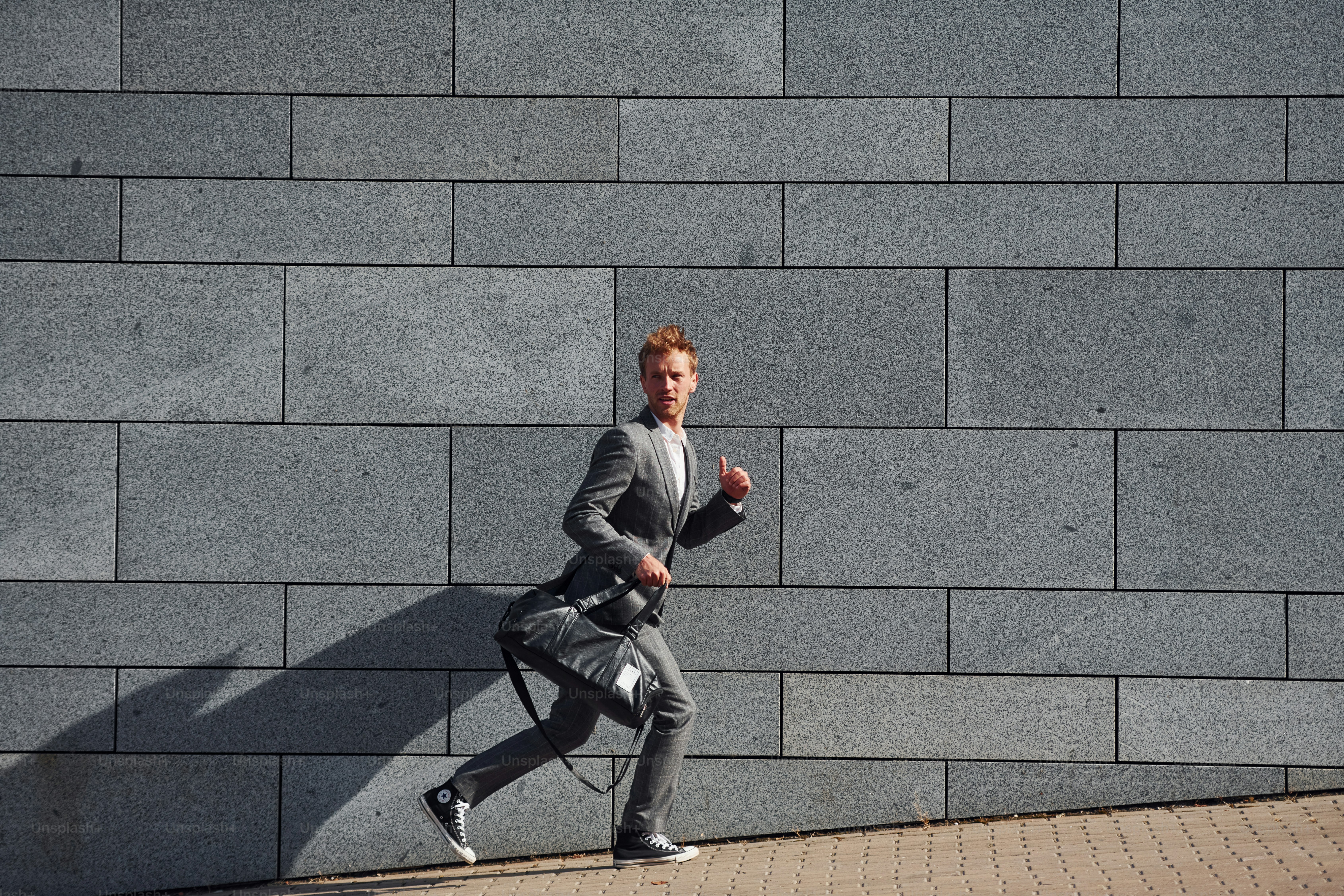 Runs and lating to the job. Young businessman in grey formal wear is outdoors in the city