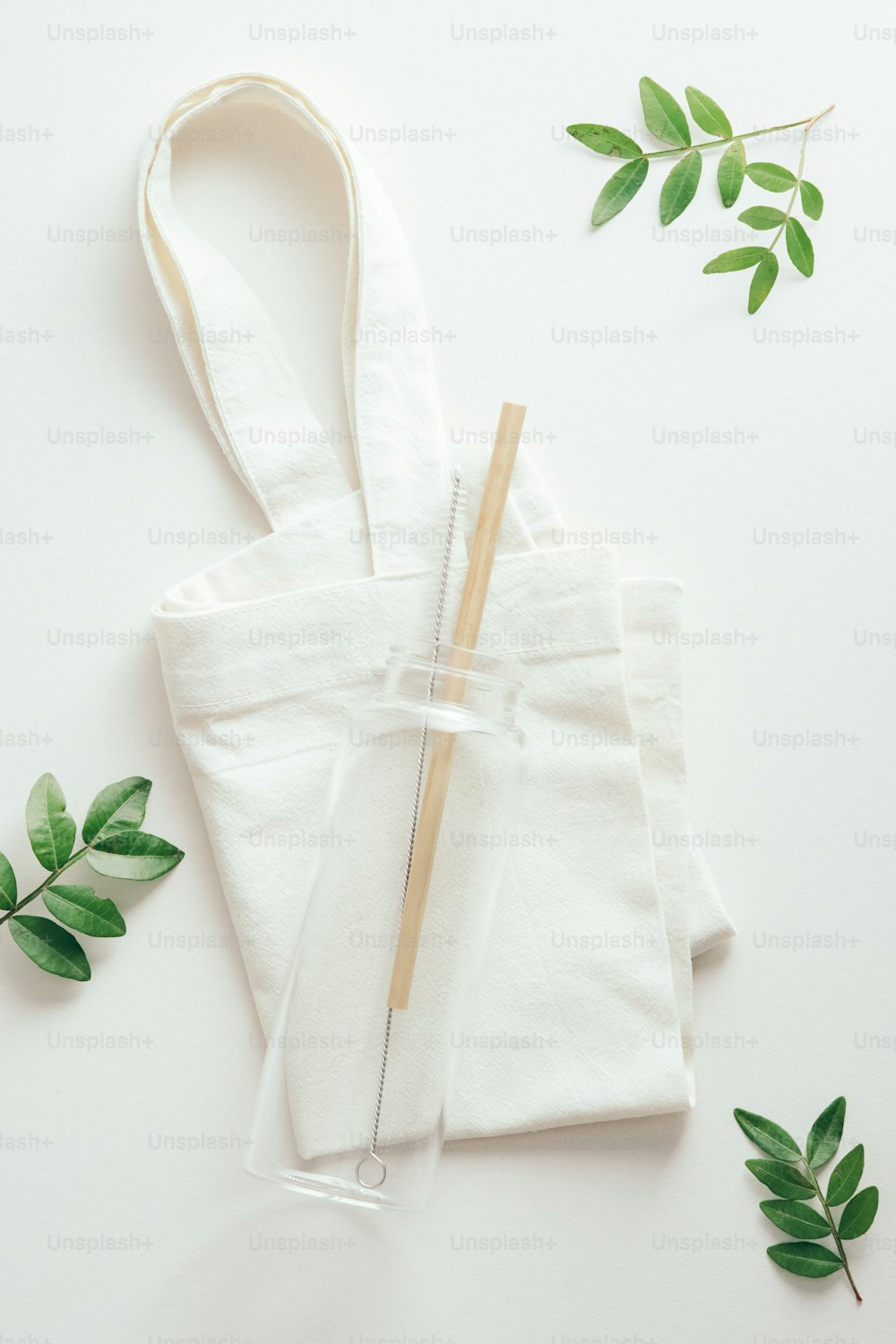 Borraccia in vetro ecologico riutilizzabile con paglia di bambù su shopper di stoffa con foglie verdi. Concetto di stile di vita sostenibile.