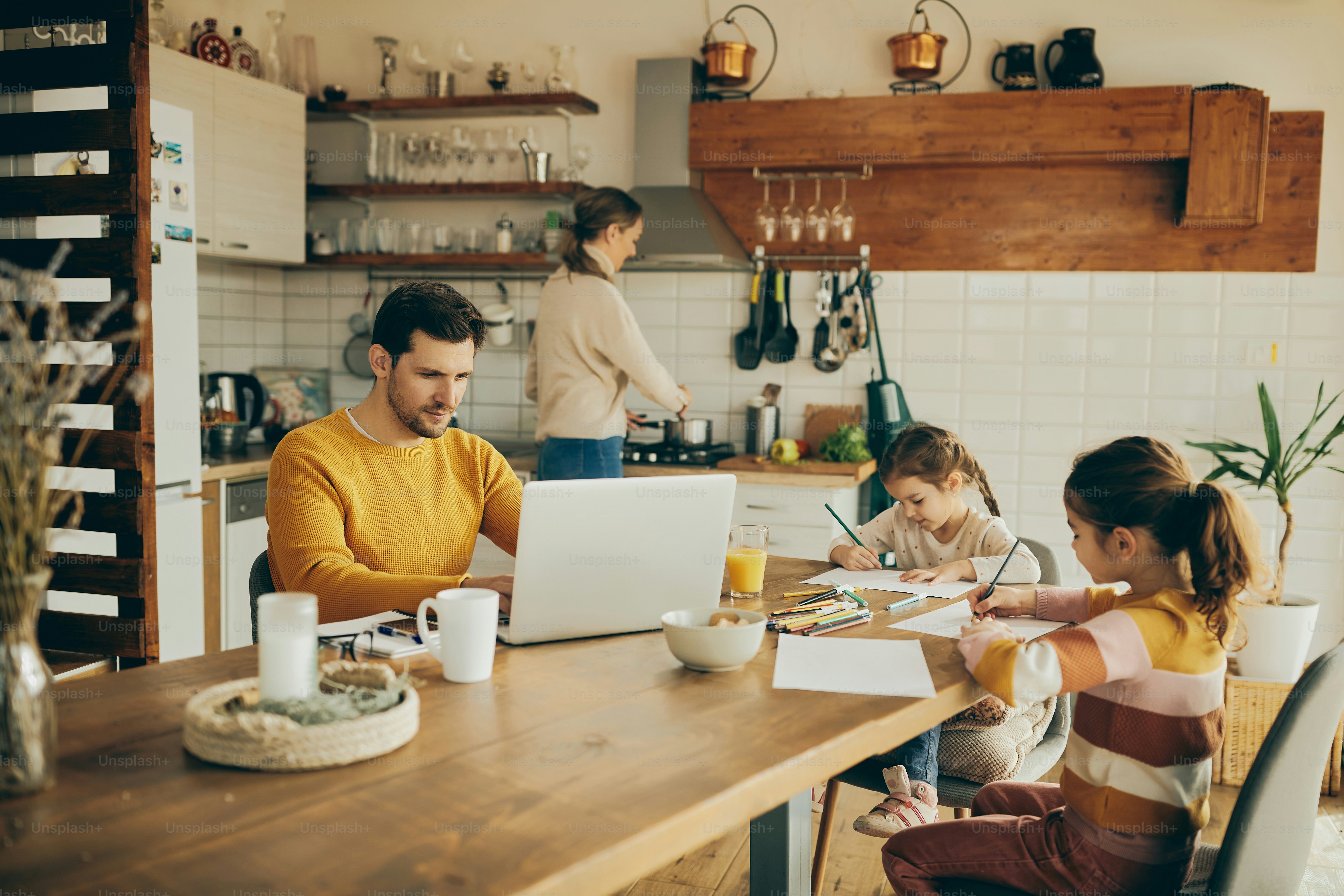Working father using computer while being with his wife and kids at home.