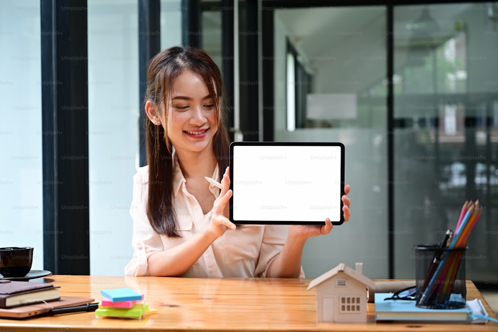 Smiling businesswoman holding mock up digital tablet with empty screen while sitting in modern office.