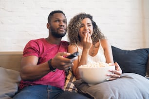Young couple spending time together and watching tv series or movies while sitting on couch at home.