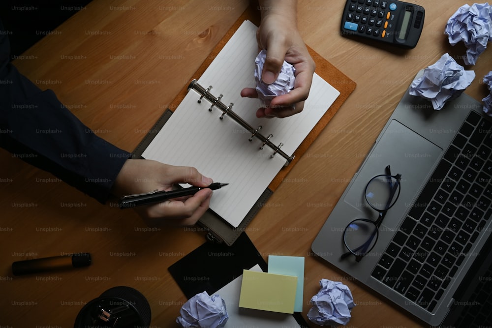 Overhead shot stressed businessman crumpling paper at office desk.