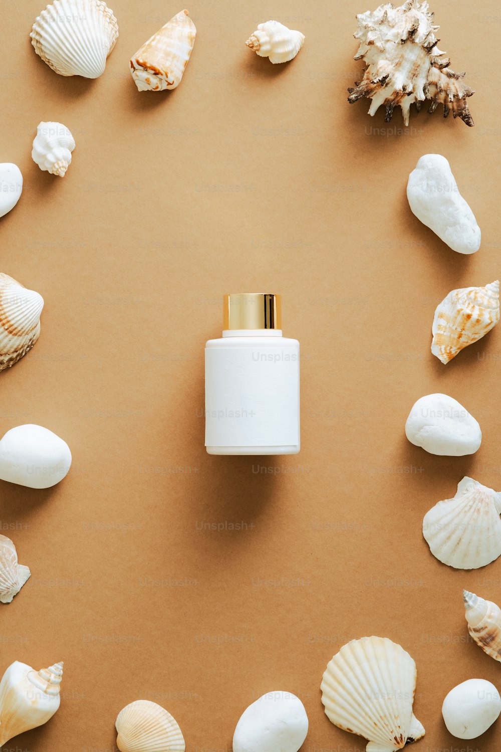 Luxury sunscreen lotion bottle and frame of seashells on sand colored background. Flat lay, top view, copy space. Beauty product packaging design.