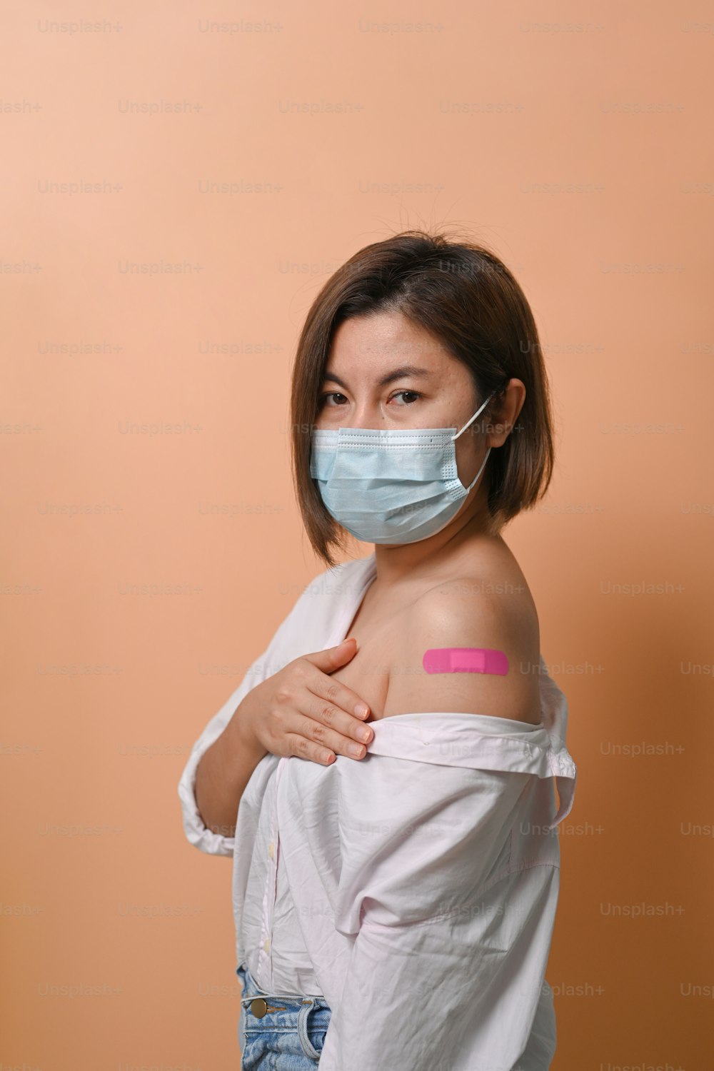 Asiatische Frau, die auf beigem Hintergrund steht und ihren Arm zeigt, nachdem sie einen Impfstoff erhalten hat.