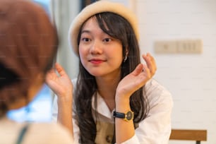 Young beautiful Asian woman friends sitting by the window in cafe with drinking fruit juice and talking together with happiness. Attractive female friendship enjoy leisure activity and meeting in the city