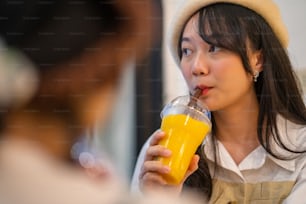 Junge schöne asiatische Freundinnen sitzen am Fenster im Café, trinken Fruchtsaft und reden glücklich miteinander. Attraktive Frauenfreundschaft genießen Freizeitaktivitäten und Treffen in der Stadt