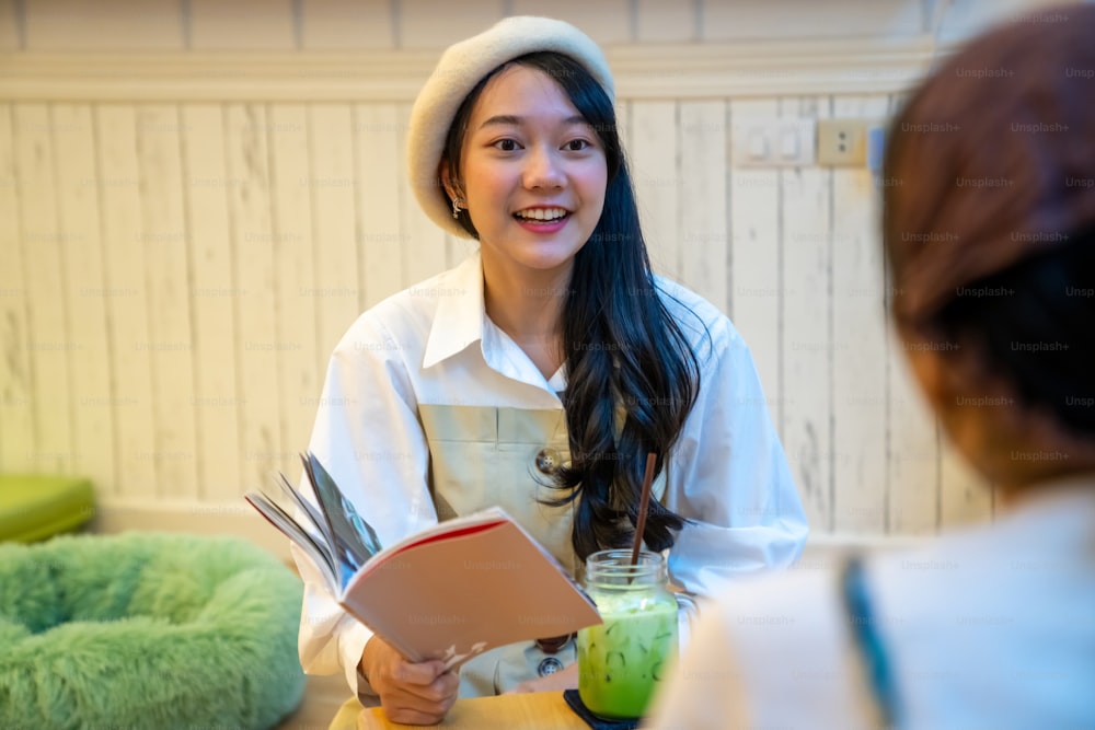 Junge schöne asiatische Freundinnen sitzen auf dem Boden im Wohnzimmer mit Eisgetränk und nehmen zusammen mit Glück. Attraktive weibliche Freundschaft genießen Freizeitaktivitäten und Begegnungen.