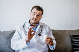 portrait latin man doctor talking online with patient, making video call, looking at camera wearing white uniform with stethoscope consulting at home in Mexico city