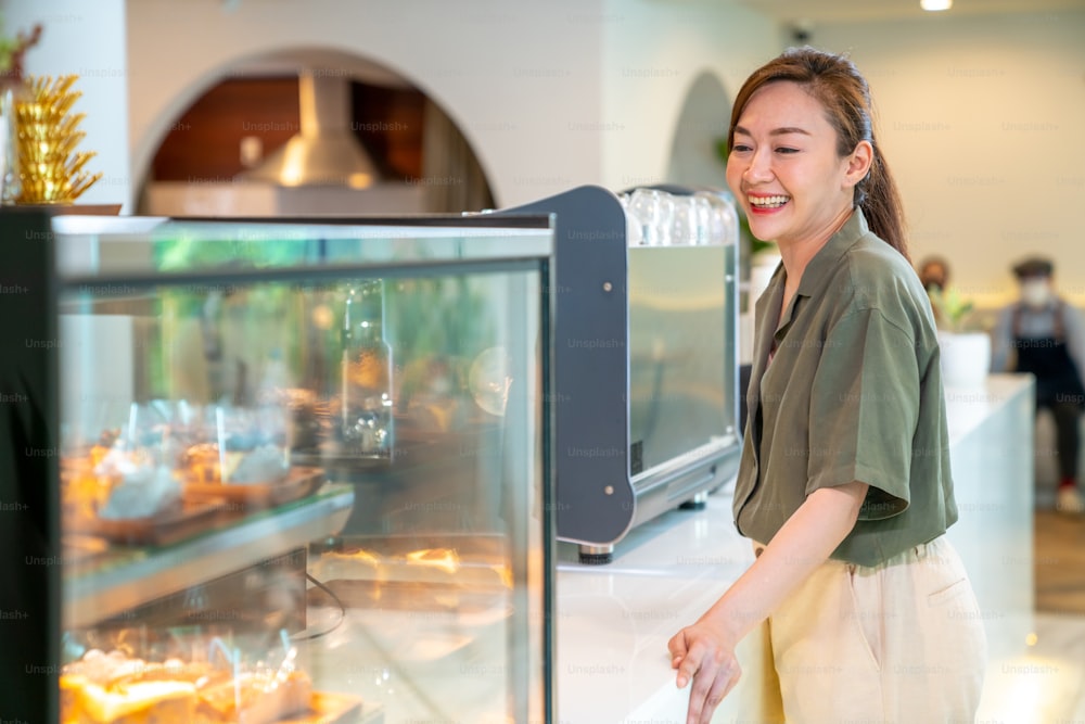 Young beautiful Asian woman coffee shop employee barista working at cafe. Smiling female cashier taking order coffee and bakery from customer. Small business owner and part time job working concept