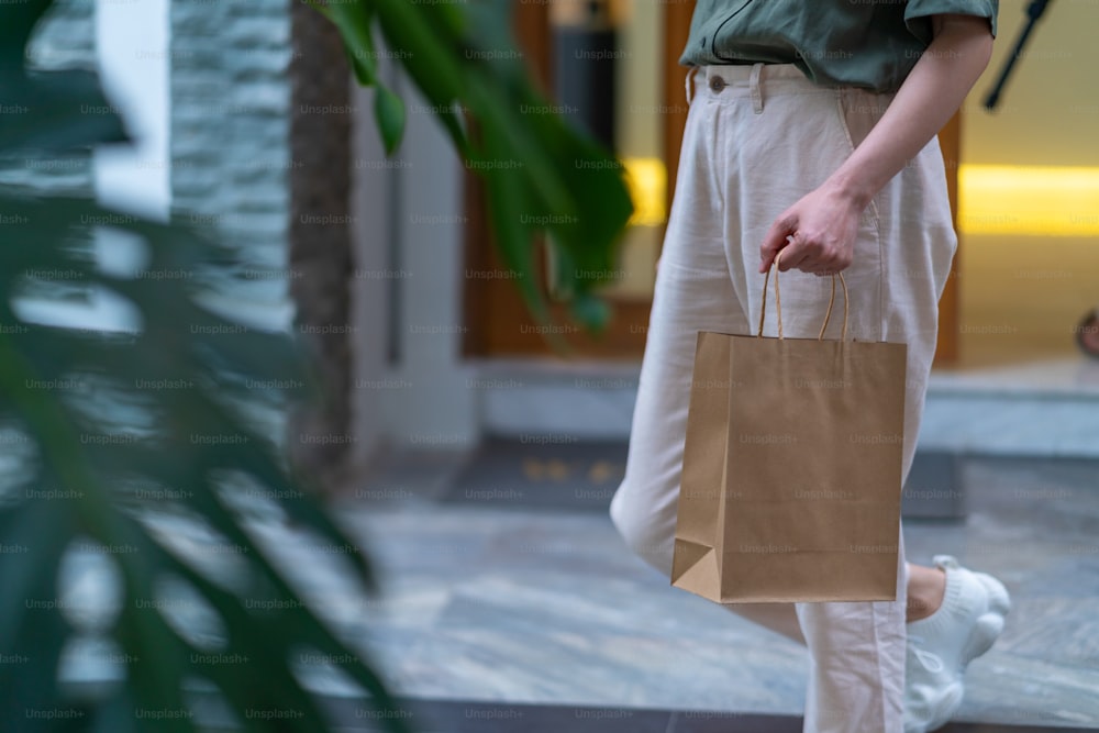 Asian woman holding takeaway order in paper shopping bag walking out of cafe. Coffee shop employee preparing takeaway order to customer. Small business owner restaurant entrepreneur and city life concept