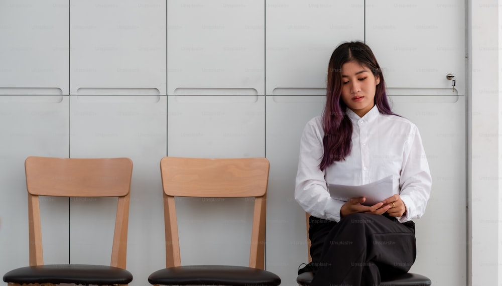 就職の面接を待っている間、書類を確認するために座っている履歴書を持つアジア人女性。