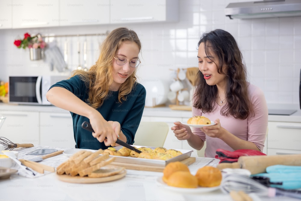 Lindas dos felices, hermosas panaderas horneando dulces Las mujeres se divirtieron en una lección de elaboración de pan y usan sus manos para golpear la masa en la cocina para hacer pasteles juntas.