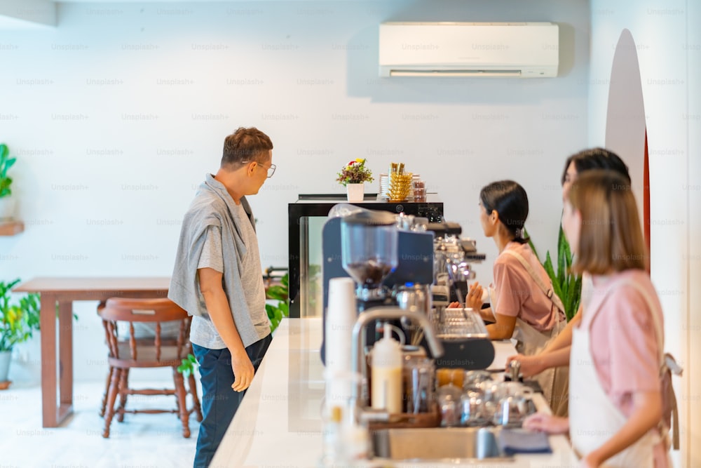 Group of Young Asian man and woman coffee shop employee working together at cafe. Female cashier taking order from customer to male barista. Small business owner and part time job working concept