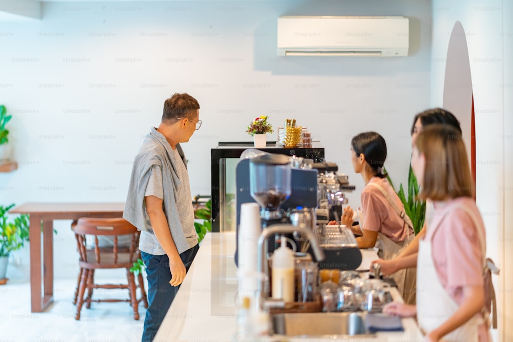 Groupe de jeunes employés asiatiques d’un café et d’une femme travaillant ensemble au café. Caissière prenant la commande du client au barista. Propriétaire d’une petite entreprise et concept de travail à temps partiel