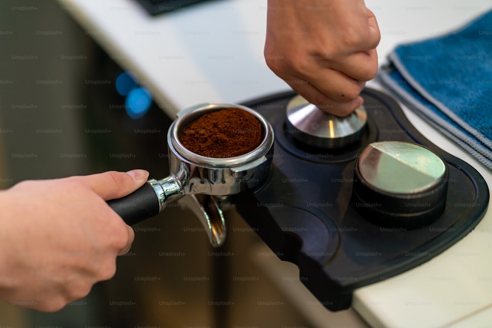 L'impiegato part-time della caffetteria dell'uomo asiatico prepara il caffè caldo in una macchina da caffè. Barista maschio che prepara l'espresso dal caffè macinato nella caffettiera. Piccolo imprenditore e concetto di lavoro part-time.