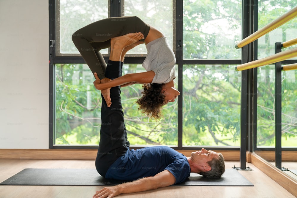 Healthy and strong couple do yoga practicing and body stretching exercise together in yoga fitness studio. Wellness man and woman relax and enjoy sport training workout and indoor activity lifestyle.