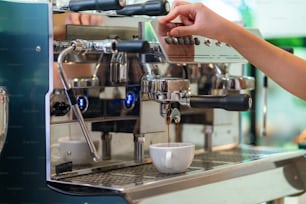 Asian man coffee shop part time employee brew hot coffee in a coffee machine. Male barista making espresso from ground coffee in coffee maker. Small business owner and part time job working concept.