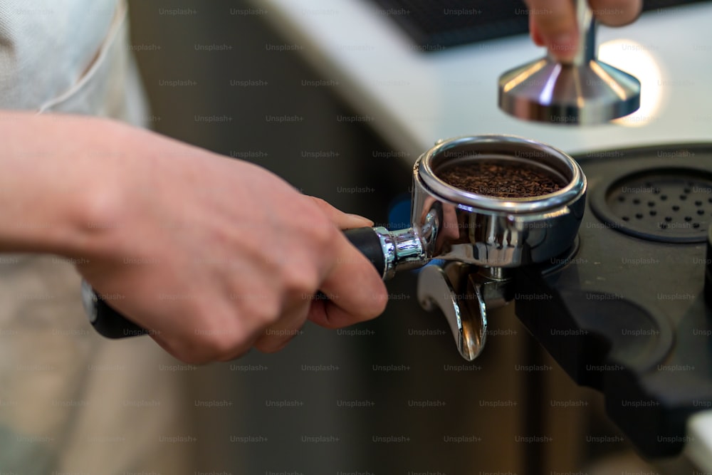 Funcionário de meio período da cafeteria asiática prepara café quente em uma máquina de café. Barista masculino fazendo café expresso a partir de café moído em cafeteira. Pequeno empresário e conceito de trabalho a tempo parcial.