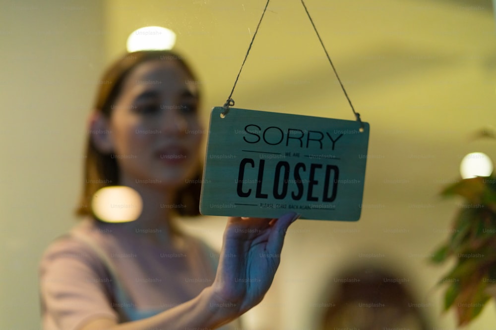 Asian woman coffee shop barista walking to cafe door and turning hanging closed sign. Female waitress preparing restaurant for service to customer. Small business owner and part time job working concept