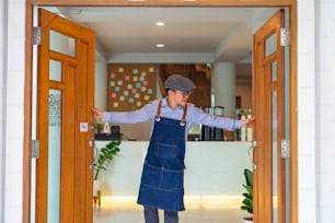 Portrait of Smiling Asian man coffee shop manager open shop door and standing with crossing arms. Male cafe owner waiting for customer with happiness. Small business restaurant entrepreneur concept