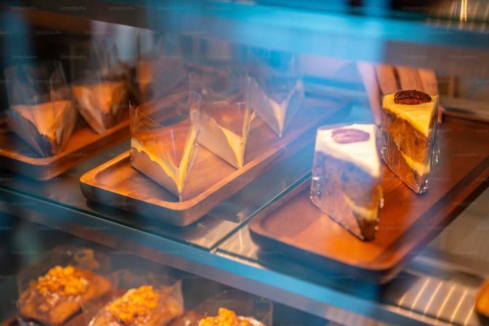 Joven empleada asiática de la cafetería que coloca pastelería y pastel en el escaparate del refrigerador de la panadería en la cafetería. Camarera preparando restaurante para el servicio al cliente. Concepto de pequeña empresa y trabajo a tiempo parcial