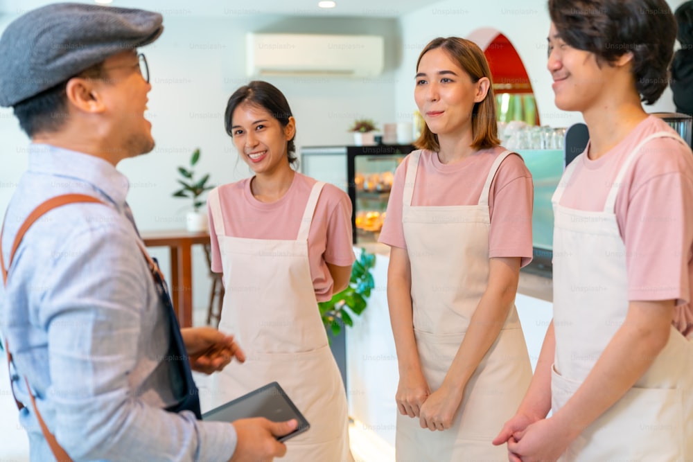 Asian male coffee shop manager briefing man and woman staff team before working. Small business cafe and restaurant owner instruct part time employee preparing service to customers before opening