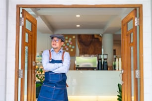 Portrait of Smiling Asian man coffee shop manager open shop door and standing with crossing arms. Male cafe owner waiting for customer with happiness. Small business restaurant entrepreneur concept